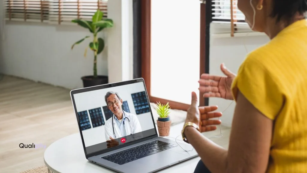 Telemedicine consultation between patient and doctor via laptop, with Qualiphy branding visible.
