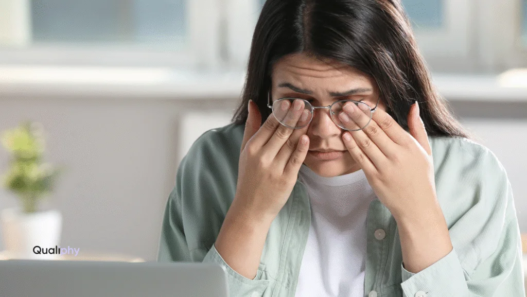 Woman rubbing her eyes during a telehealth consultation, showing symptoms of pink eye (conjunctivitis). Qualiphy provides same-day telehealth urgent care with prescription pick-up for pink eye and other common conditions.