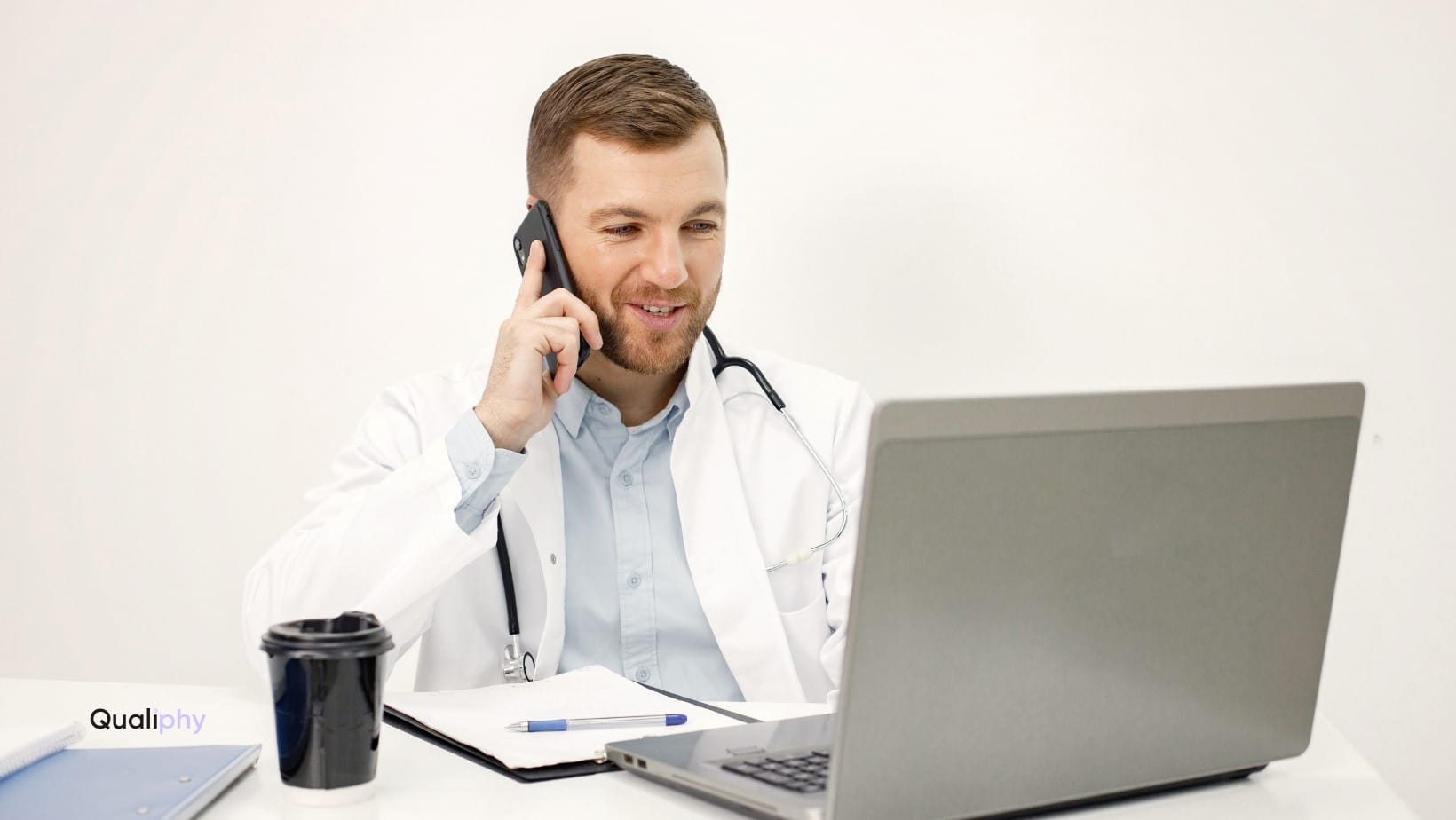 A healthcare provider conducting an on-demand telehealth consultation on a laptop while speaking on the phone, demonstrating an alternative to remote patient monitoring for home health in med spa settings.