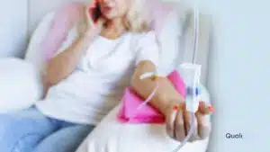 A woman receiving an IV drip while on the phone, illustrating the importance of IV therapy compliance in clinics to ensure treatments are safely administered by qualified providers